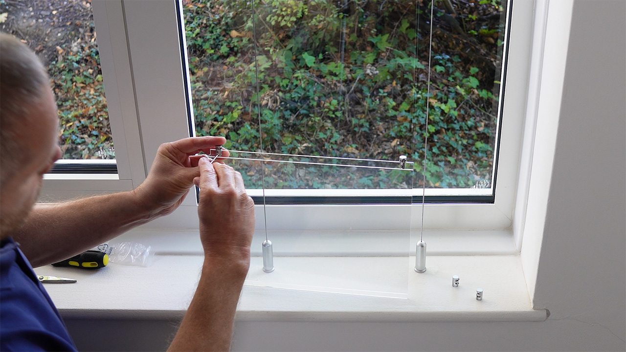 Using an Allen key to attach four panel clamps to an acrylic poster pocket, one at each corner.