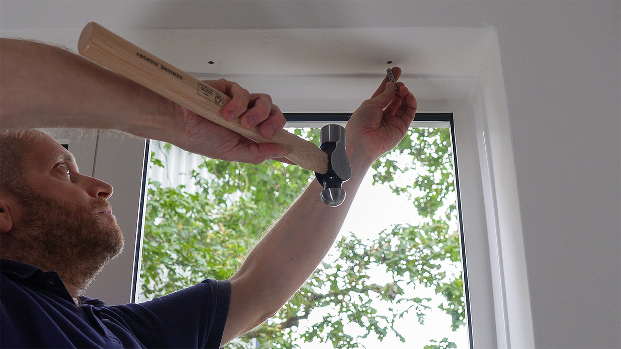 Gently hammering a plastic fixing plug into a drilled hole.