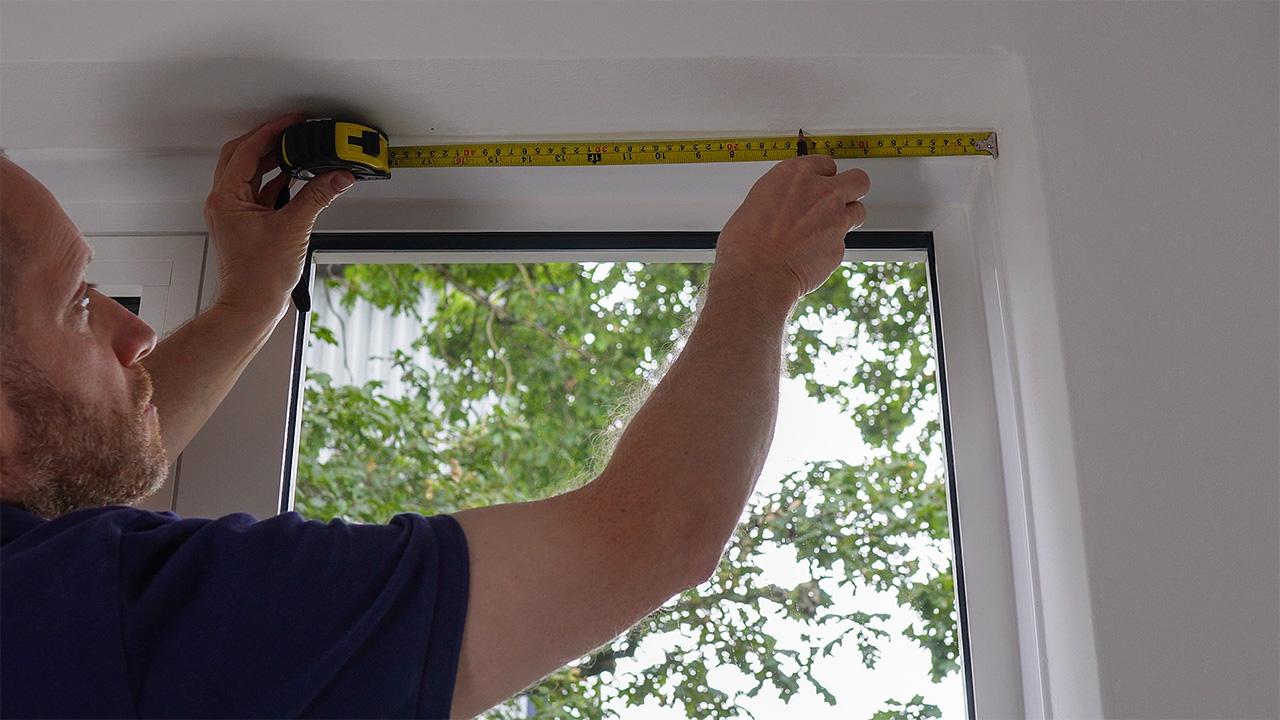 Tape measuring the hole centres for the top fixings of a cable-suspended LED light-pocket display kit.