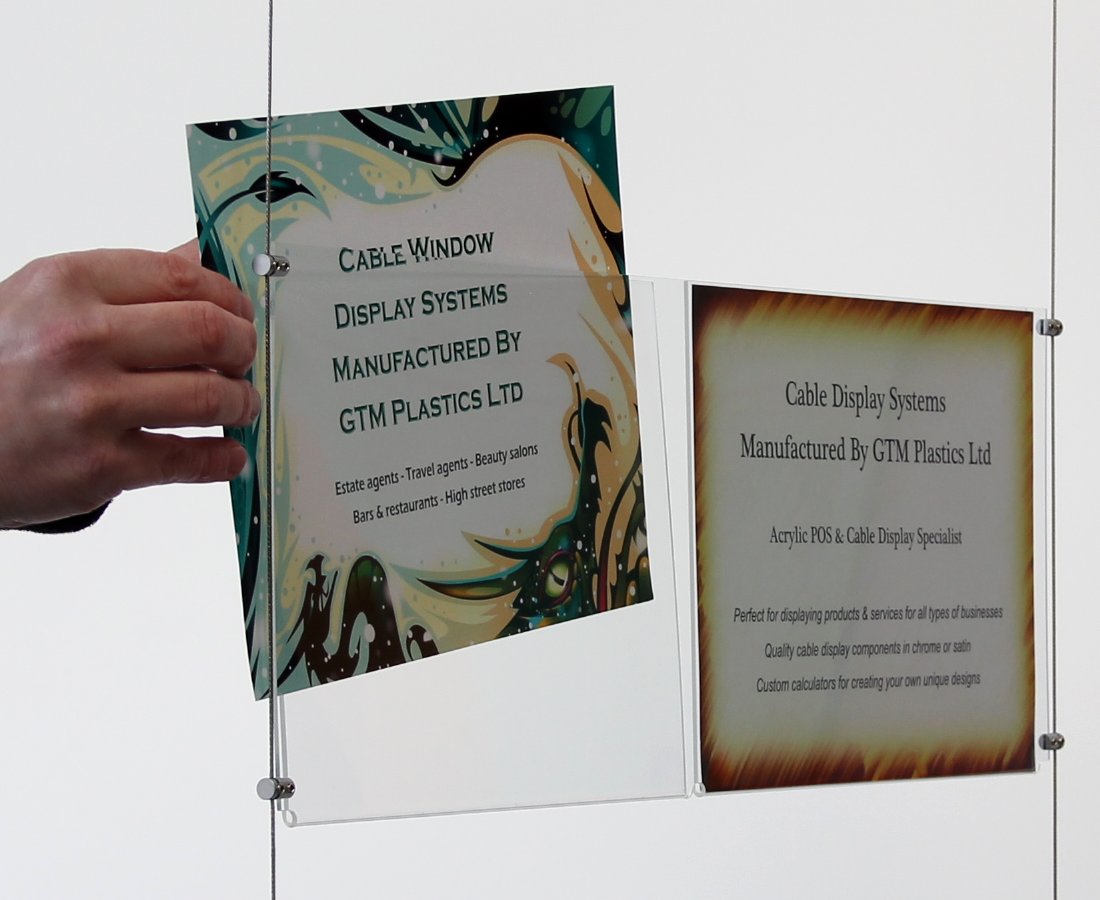 A closeup view of one double-width landscape acrylic poster pocket, suspended between two cables, showing a person’s hand removing one of the posters.